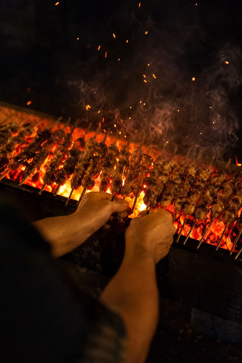 Grill cook turning skewers over charcoal